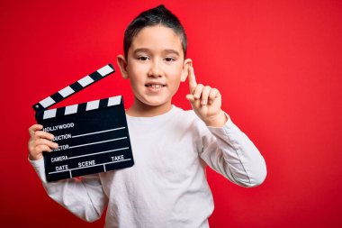 Küçük çocuk video kaydediyor. Sinema direktörü, kırmızı arka plan üzerinde. Bir fikir ya da soru işareti ile şaşırdı.