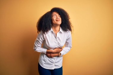Afro saçı sarı arka planda ayakta duran güzel Afro-Amerikan zarif genç bir kadın midenin üstünde duruyor çünkü hazımsızlık, acı verici bir hastalık kendini iyi hissetmiyor. Ache kavramı.
