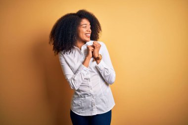 Afro saçlı, sarı arka planda dikilen, elleri çenesinde gergin ve heyecanlı genç, Afro-Amerikan zarif bir kadın.