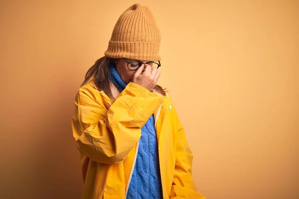 黄色のレインコートと冬の帽子を身に着けている中年の女性は 孤立した背景に疲れ鼻と目をこすり疲労と頭痛を感じている ストレスとフラストレーションの概念 — ストック写真