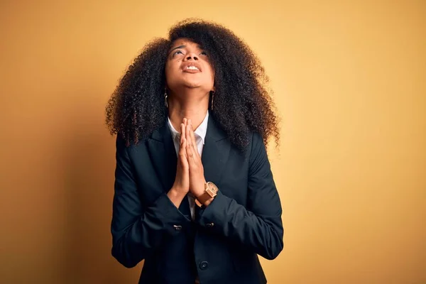 Young beautiful african american business woman with afro hair wearing elegant jacket begging and praying with hands together with hope expression on face very emotional and worried. Begging.