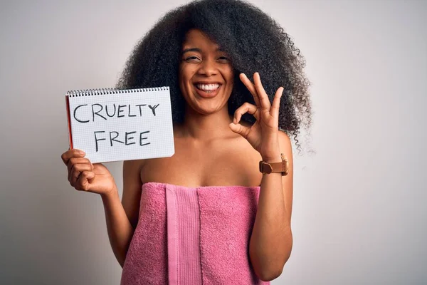 Young african american woman with afro hair wearing a towel asking for cruelty free beauty doing ok sign with fingers, excellent symbol