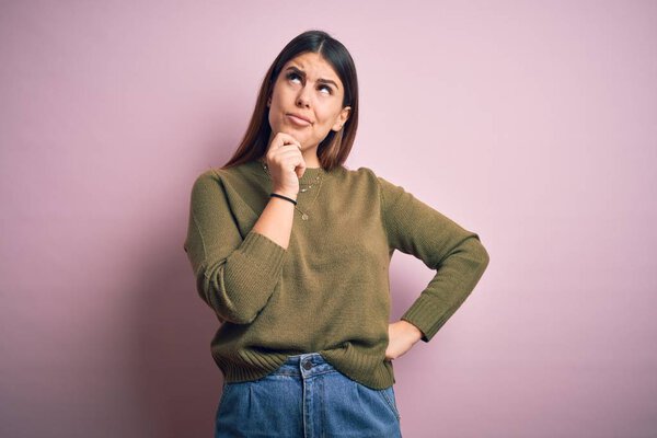 Young beautiful woman wearing casual sweater standing over isolated pink background with hand on chin thinking about question, pensive expression. Smiling with thoughtful face. Doubt concept.