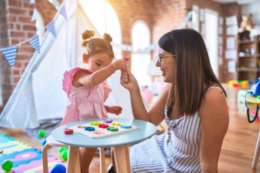 Anaokulunda rakamlarla oynayan genç ve güzel bir öğretmen ve çocuk matematik öğreniyor.