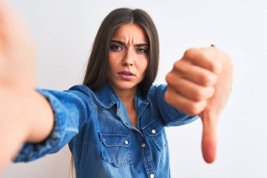 Kot gömlek giyen güzel bir kadın, izole edilmiş beyaz arka planda kamerayla selfie çekiyor. Mutsuz ve kızgın görünüyor. Reddedildiğini gösteriyor. Kötü ifade.