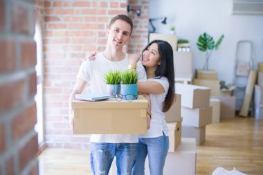 Young beautiful couple sitting on the floor at new home around cardboard boxes celebrating surprised and amazed for success with arms raised and open eyes. Winner concept.