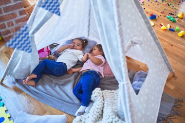 Sevimli bebekler çadırın içinde battaniyeye uzanıp gülüyorlar ve anaokulunda oyuncak bebekle oynuyorlar.