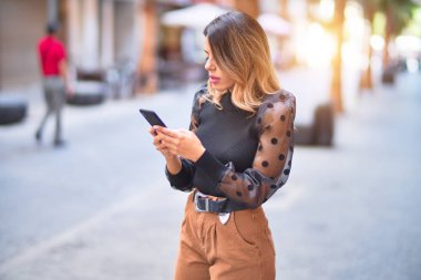 Young beautiful woman smiling happy and confident. Standing using smartphone at town street