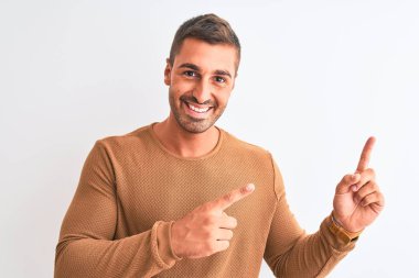 Kışlık süveter giyen yakışıklı, soyutlanmış arka planda gülümseyen ve kameraya bakan genç bir adam. İki eliyle ve parmaklarıyla yan tarafa bakıyor..