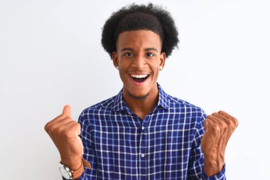Genç Afro-Amerikalı bir adam, günlük gömleğini giymiş, izole edilmiş beyaz arka planda dikiliyor. Kollarını kaldırıp, gözlerini açarak başarıyı kutluyor ve şaşırıyor. Kazanan konsept.