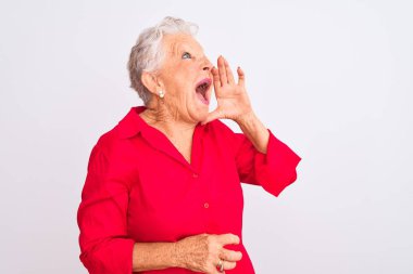 Senior grey-haired woman wearing red casual shirt standing over isolated white background shouting and screaming loud to side with hand on mouth. Communication concept.