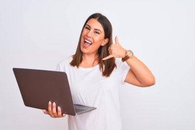 Güzel genç bir kadın bilgisayarını beyaz arka plan üzerinde kullanıyor gülümsüyor telefonla el ve parmaklarıyla telefon hareketi yapıyor telefonda konuşuyor gibi. İletişim kavramları.