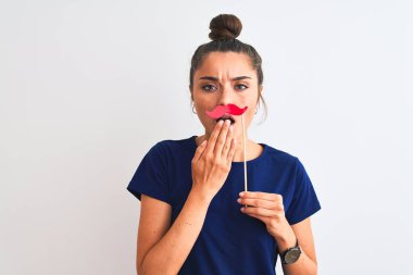 Young beautiful woman holding fanny party mustache over isolated white background cover mouth with hand shocked with shame for mistake, expression of fear, scared in silence, secret concept