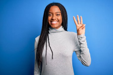 Young african american woman standing wearing casual turtleneck over blue isolated background showing and pointing up with fingers number three while smiling confident and happy.