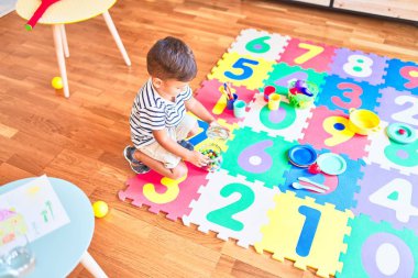 Güzel çocuk bulmacanın üzerinde oturmuş anaokulunda küçük renkli çikolata topları yiyor.