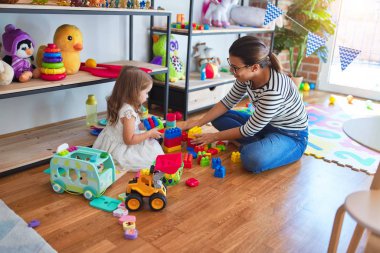 Güzel öğretmen kadın ve bebek anaokulunda bir sürü oyuncağın etrafında taşlarla oynuyorlar.