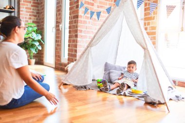 Güzel öğretmen ve küçük çocuk yerde oturup anaokulunda içeride oynuyorlar.