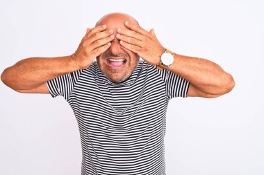 Orta yaşlı yakışıklı adam izole edilmiş beyaz arka plan üzerine çizgili donanma tişörtü giyiyor gözleri kapayıp neşeli ve komik gülümsüyor. Kör kavram.