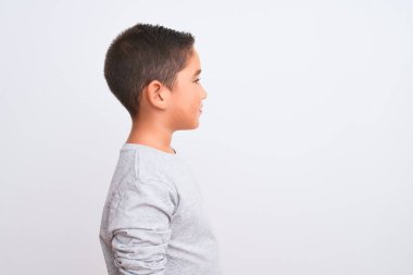 Beautiful kid boy wearing grey casual t-shirt standing over isolated white background looking to side, relax profile pose with natural face with confident smile.