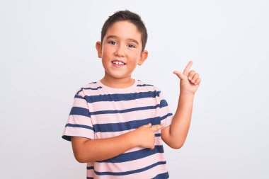Beautiful kid boy wearing casual striped t-shirt standing over isolated white background with a big smile on face, pointing with hand and finger to the side looking at the camera.