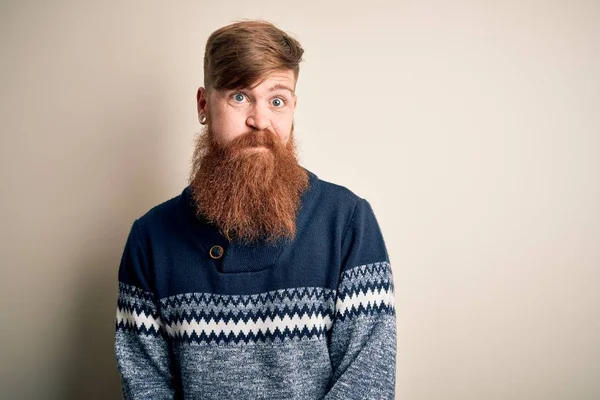 ひげを生やしたハンサムなアイルランドの赤毛の男は 孤立した背景に冬のセーターを着て 面白い顔で頬をむいています 口は空気で膨脹し 狂気の表現 — ストック写真