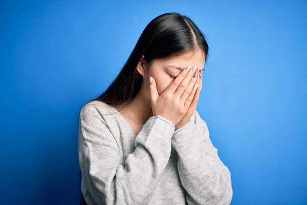泣きながら手で顔を覆う悲しい表情で青い孤立した背景の上に立つカジュアルなセーターを着た若い美しいアジアの女性 うつ病の概念 — ストック写真