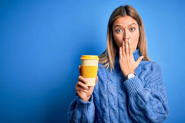 Young beautiful woman holding take away glass of coffee over isolated blue background cover mouth with hand shocked with shame for mistake, expression of fear, scared in silence, secret concept