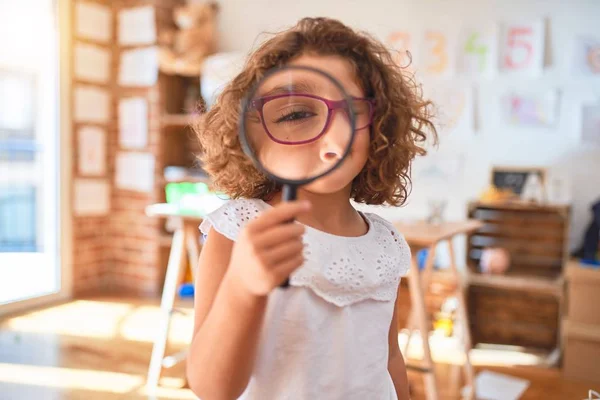 Beautiful toddler standing  wearing glasses using loupe at kindergarten