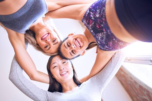 Young beautiful group of sportswomen smiling happy. Standing hugging with smile on face after class of yoga at gym