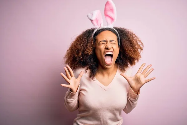 年轻的非洲裔美国女人 有着一头黑发 长着兔子般的耳朵 粉红的背景 欢庆疯狂和疯狂的成功 举起双臂 紧闭的眼睛兴奋地尖叫着 赢的概念 — 图库照片