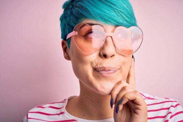 Молодая красивая женщина с голубыми волосами моды носить поясные очки с сердцем серьезное лицо, думая о вопросе, очень запутанная идея
