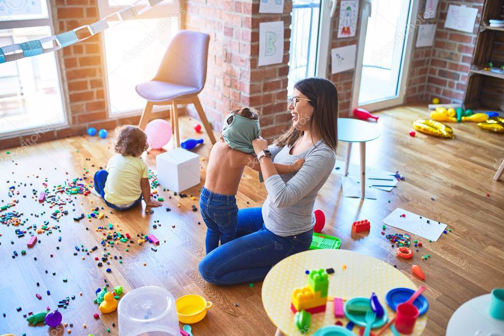 Young beautiful teacher and toddlers playing at kindergarten