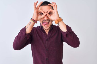 Tecrit edilmiş arka planda duran genç yakışıklı iş adamı dürbün gibi jest yapıyor, gözleri parmaklarından bakıyor. Çılgın ifade.