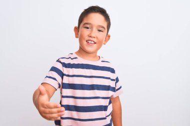 Beautiful kid boy wearing casual striped t-shirt standing over isolated white background smiling friendly offering handshake as greeting and welcoming. Successful business.