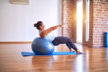 Orta yaşlı güzel sporcu kadın mutlu gülümsüyor. Spor salonunda yoga sınıfında spor topu kullanarak esneme hareketi.