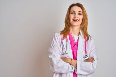 Redhead caucasian doctor woman wearing pink stethoscope over isolated background happy face smiling with crossed arms looking at the camera. Positive person.