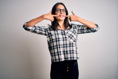 Young brunette woman with blue eyes wearing casual shirt and glasses over white background smiling cheerful showing and pointing with fingers teeth and mouth. Dental health concept.