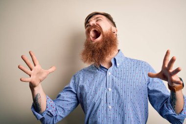 Handsome Irish redhead business man with beard standing over isolated background crazy and mad shouting and yelling with aggressive expression and arms raised. Frustration concept.