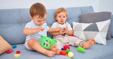 Güzel bebekler, biri ağlıyor, kanepede oturuyor, evde oyuncaklarla oynuyor.