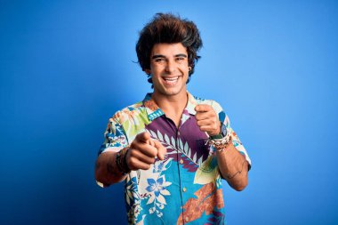 Young handsome man on vacation wearing summer shirt over isolated blue background pointing fingers to camera with happy and funny face. Good energy and vibes.