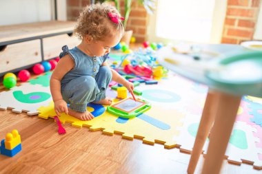 Renkli oyun odasında beyaz güzel bir bebek oyuncaklarla oynuyor. Anaokulunda mutlu ve şen şakrak.