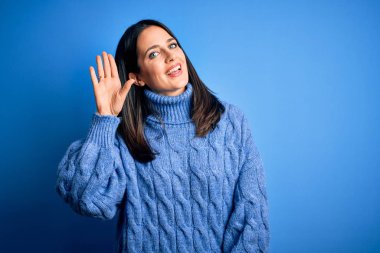 Young brunette woman with blue eyes wearing casual turtleneck sweater Waiving saying hello happy and smiling, friendly welcome gesture