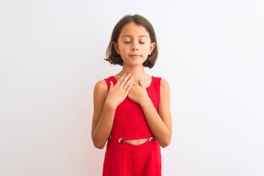 İzole edilmiş beyaz arka planda kırmızı bir elbise giyen genç ve güzel bir kız çocuğu. Elleri göğsünde, gözleri kapalı bir şekilde gülümsüyor ve yüzünde minnet ifadesi var. Sağlık kavramı.