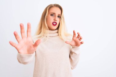 Young beautiful woman wearing turtleneck sweater standing over isolated white background afraid and terrified with fear expression stop gesture with hands, shouting in shock. Panic concept.