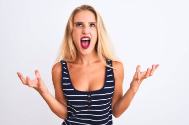 Young beautiful woman wearing casual striped t-shirt standing over isolated white background crazy and mad shouting and yelling with aggressive expression and arms raised. Frustration concept.