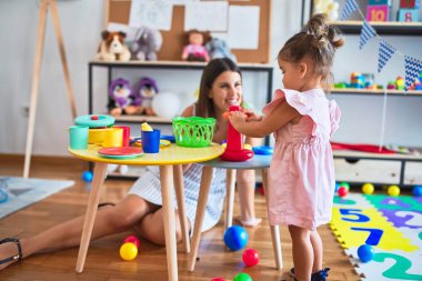 Genç, güzel öğretmen ve bebek, anaokulundaki masada halkalar kullanarak piramit inşa ediyorlar.