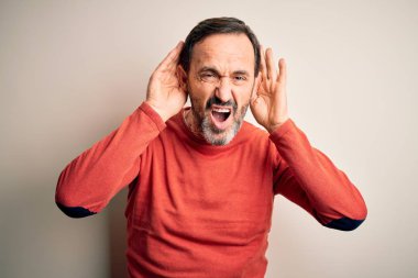 Orta yaşlı, turuncu süveter giyen, izole edilmiş beyaz arka planda dikilen, iki elini de kulak hareketi yaparken duymaya çalışan, dedikoduya meraklı, orta yaşlı bir adam. İşitme problemi, sağır