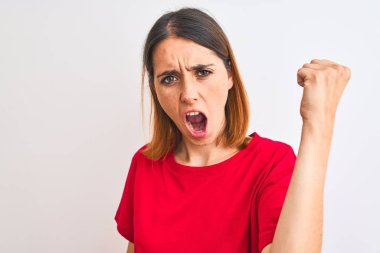 Beautiful redhead woman wearing casual red t-shirt over isolated background angry and mad raising fist frustrated and furious while shouting with anger. Rage and aggressive concept.