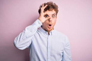 Sarışın, kıvırcık saçlı, beyaz arka planda çizgili tişört giyen, şaşırmış yüzüyle şaşırmış, parmaklarından bakan genç, yakışıklı bir adam. İnançsız ifade.