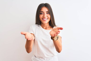 Young beautiful woman wearing casual t-shirt standing over isolated white background smiling cheerful offering hands giving assistance and acceptance.